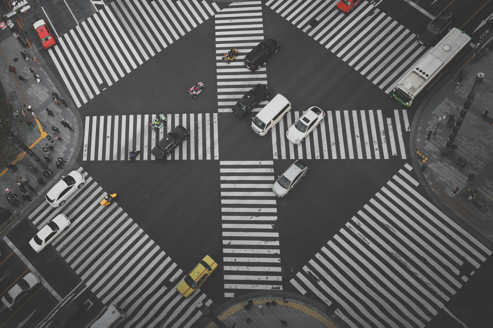 Overhead view of cars crossing a city intersection with zebra crossings, in black and white